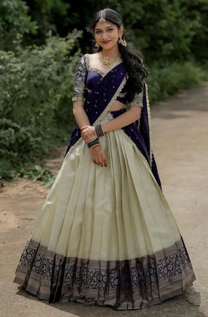 Young woman in a designer cream and navy blue half saree with zari border lehenga, embroidered blouse and sheer navy voni — custom tailoring Chennai